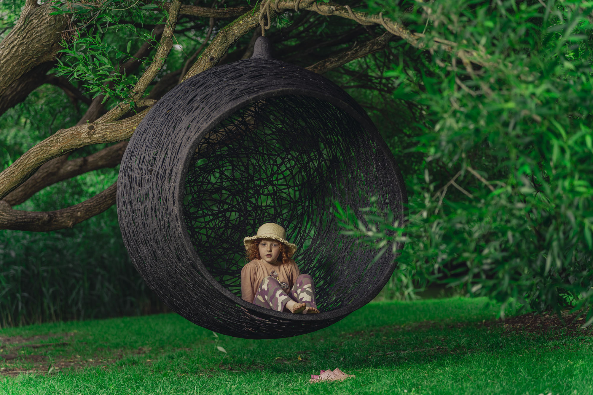 a girl sitting in a round black sofa hanging from a tree